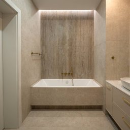 Royal Design Projektowanie Wnętrz Joanna Kowalska - Elegancka łazienka w beżach: wanna obudowana płytkami, złota armatura, oświetlenie LED. Minimalistyczny design z dbałością o detale i spójną kolorystykę.
