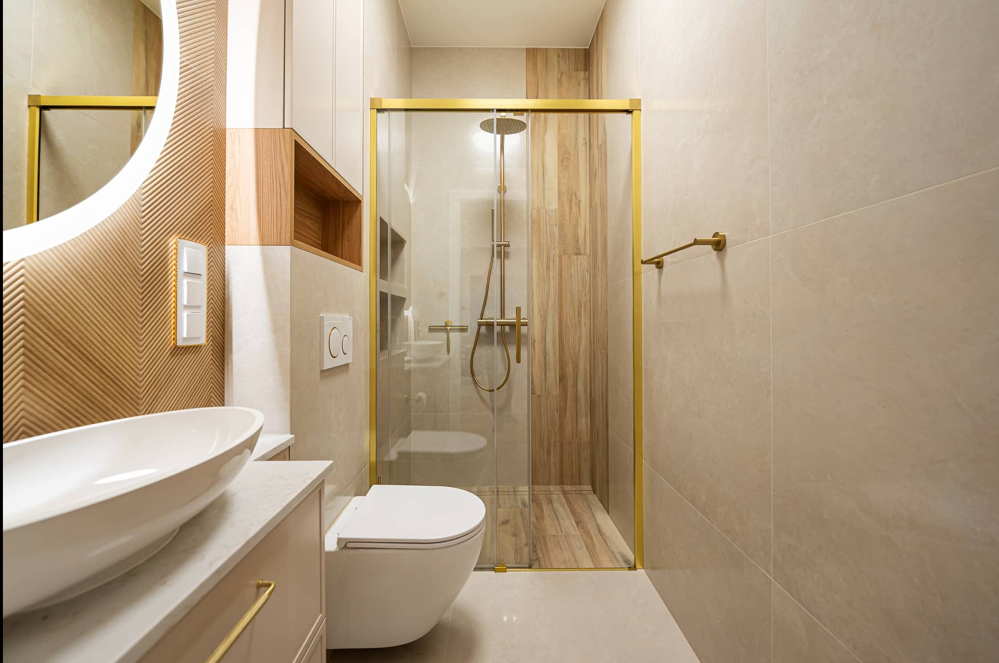 Nowoczesna łazienka z kabiną prysznicową w złotej ramie, umywalką nablatową i drewnianymi akcentami na ścianie. Minimalistyczny design z dbałością o detale.