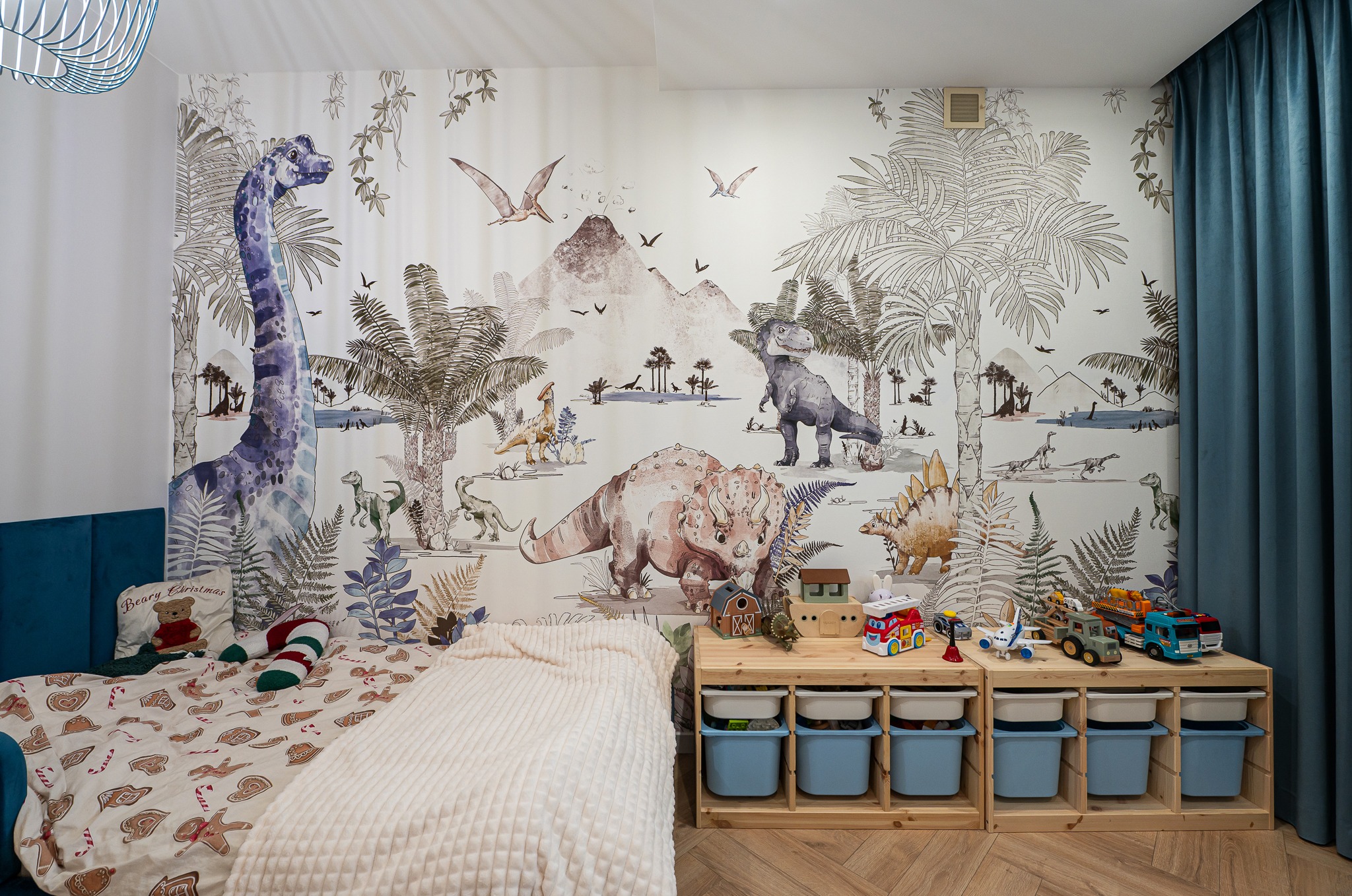 Pokój dziecięcy z łóżkiem, regałem na zabawki i tapetą w dinozaury. Motyw dżungli i prehistorycznych zwierząt tworzy unikalny klimat.
