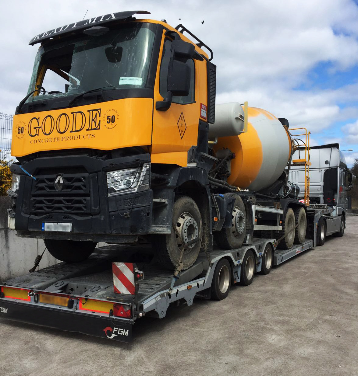 Żółto-czarna betoniarka z logo 'GOODE' transportowana na niskopodwoziowej lawecie. Widoczne zabezpieczenia ładunku i tablica ostrzegawcza.