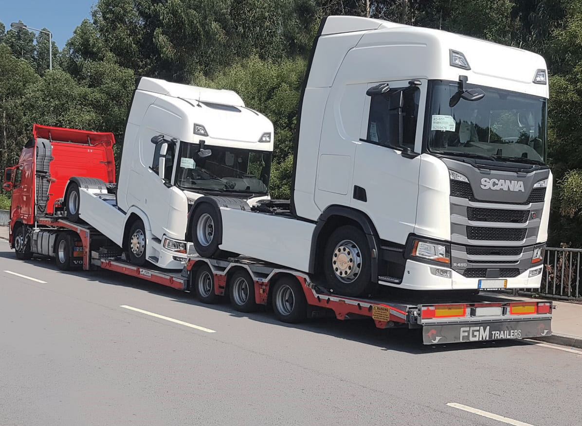 Laweta transportuje dwie białe kabiny ciężarówek Scania w Sobolewie; czerwona ciężarówka ciągnie naczepę z ładunkiem.