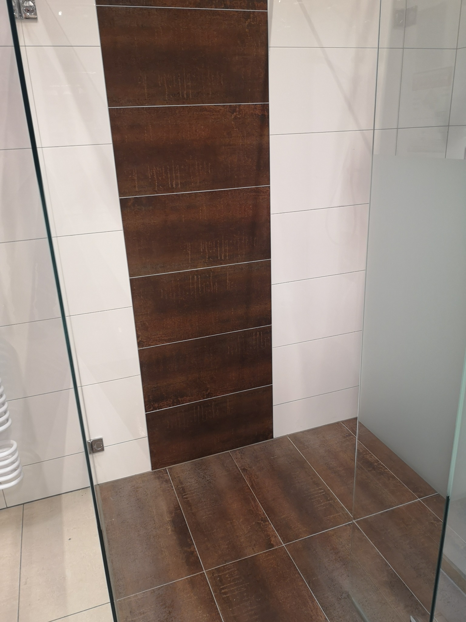 Kabina prysznicowa z brązowymi i białymi płytkami, widoczne detale wykończenia i szklane elementy.