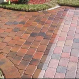 Czerwono-brązowa kostka brukowa ułożona w jodełkę, z fragmentem wyczyszczonej powierzchni, ukazująca różnicę w kolorze i wyglądzie.