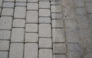 Szara kostka brukowa ułożona w regularny wzór, widoczna różnica w czystości powierzchni między ułożoną a nieułożoną częścią.