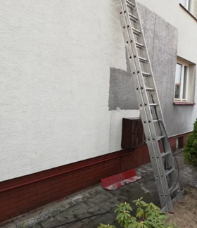 Fragment ściany budynku z nałożonym tynkiem strukturalnym, widoczny obszar w trakcie prac, oparta drabina aluminiowa.