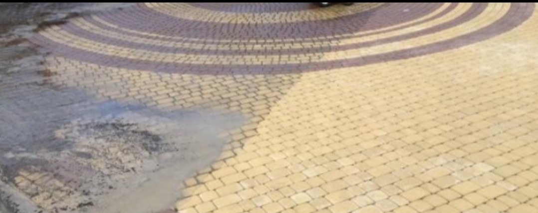 Oczyszczona pod ciśnieniem część okrągłego podjazdu z kostki brukowej w odcieniach beżu i brązu, kontrastująca z brudną, nieumytą powierzchnią.