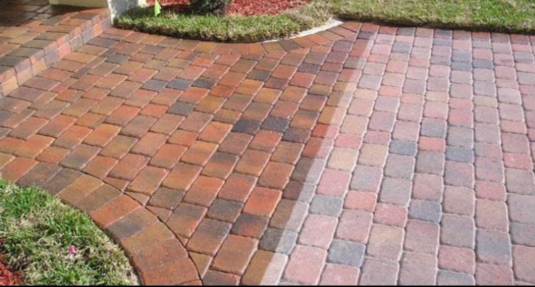 Czerwono-brązowa kostka brukowa ułożona w jodełkę, z fragmentem wyczyszczonej powierzchni, ukazująca różnicę w kolorze i wyglądzie.