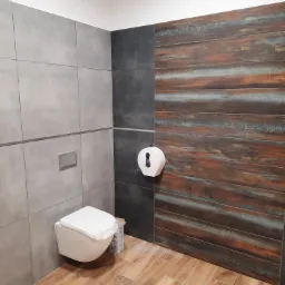 Nowoczesna łazienka z wiszącą toaletą, szarą płytką ścienną, akcentem z płytek imitujących drewno i podłogą z drewnopodobnych paneli; widoczny dozownik papieru i żółta ścierka na podłodze.