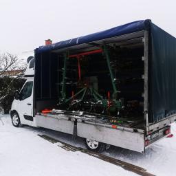 G. S. M. Transport - Ciężarówka z otwartą plandeką, załadowana zielonym sprzętem rolniczym, stoi na śniegu w pochmurny dzień.