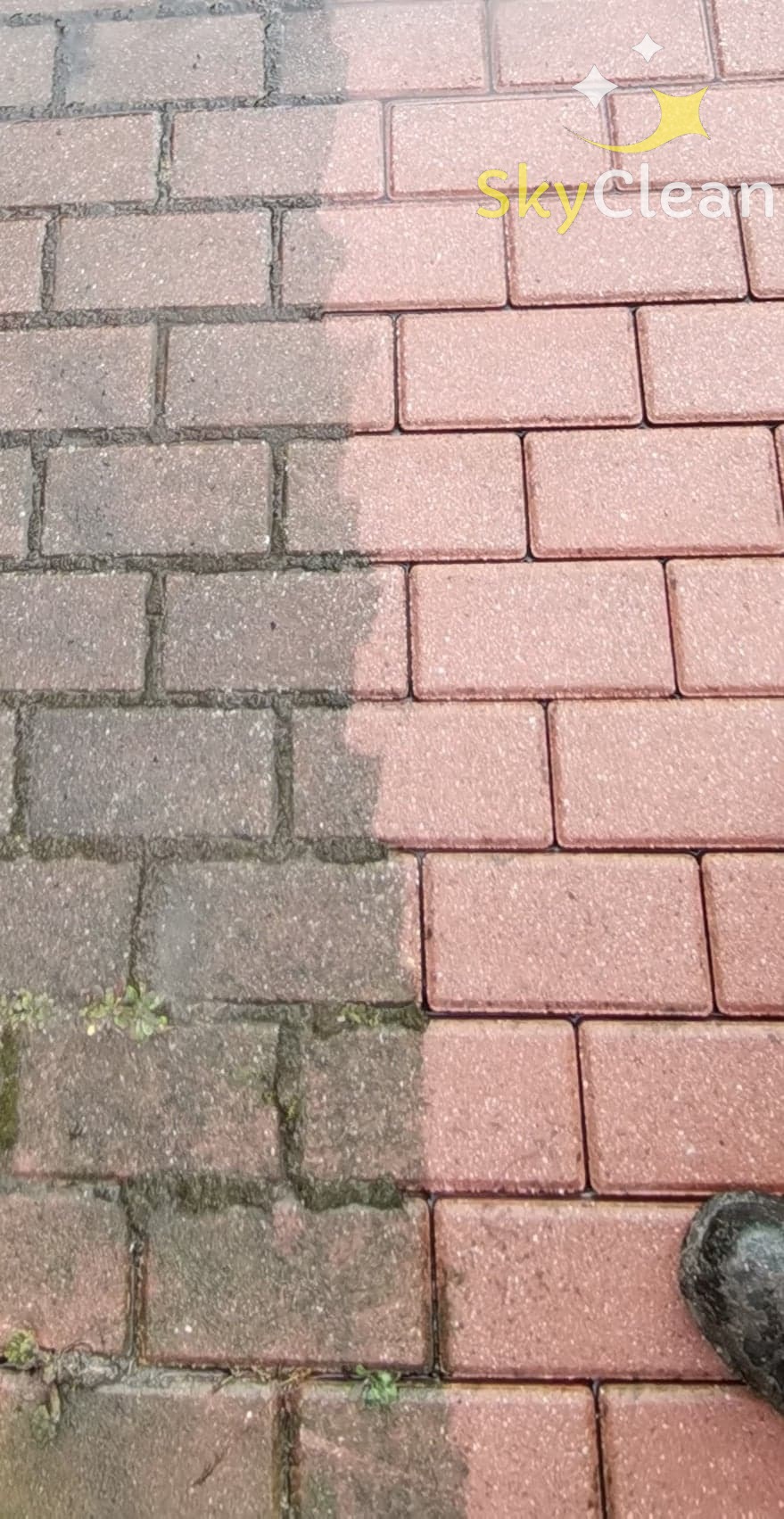 Częściowo wyczyszczona kostka brukowa w kolorze ceglastym, widoczna różnica między brudną, ciemną powierzchnią z mchem a czystą, jaśniejszą częścią, logo firmy SkyClean w prawym górnym rogu.