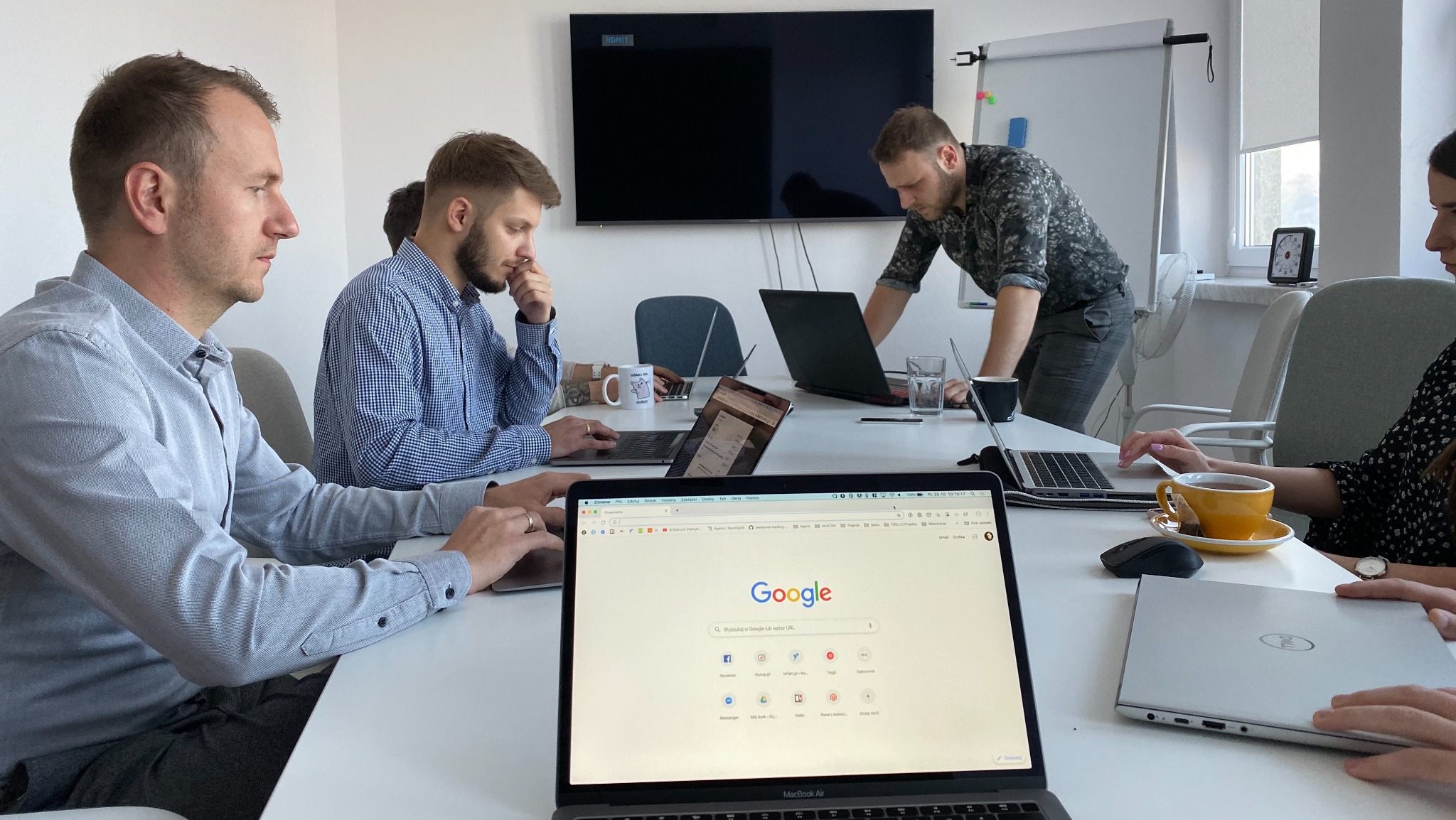Zespół ludzi pracuje przy laptopach w biurze, na jednym z ekranów widoczna strona wyszukiwarki Google.