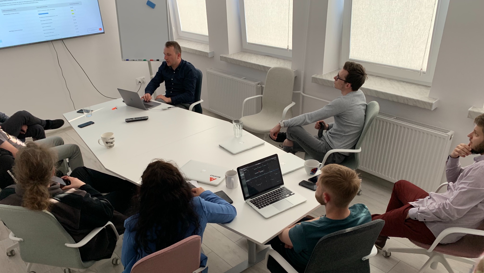 Zespół programistów podczas spotkania w biurze, omawiający projekt na ekranie i laptopach.