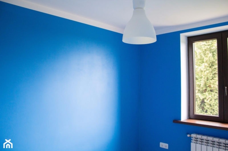 Pokój po remoncie: ściany pomalowane na intensywny niebieski kolor, biały sufit z lampą w kształcie dzwonu, okno z brązową ramą i grzejnik pod nim.