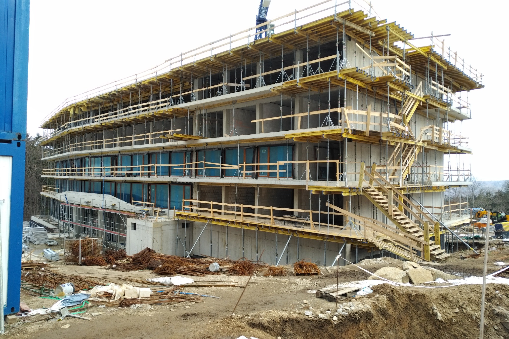Wrocław: Budowa wielopiętrowego budynku w stanie surowym, widoczne szalunki, rusztowania i zbrojenia, teren budowy z hałdami ziemi i porozrzucanymi materiałami.