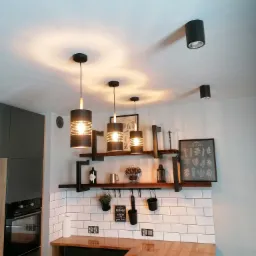 Nowoczesne oświetlenie kuchni: trzy lampy wiszące z ażurowymi kloszami i dwie lampy sufitowe punktowe, zamontowane na białym suficie w kuchni z drewnianym blatem i białymi płytkami.