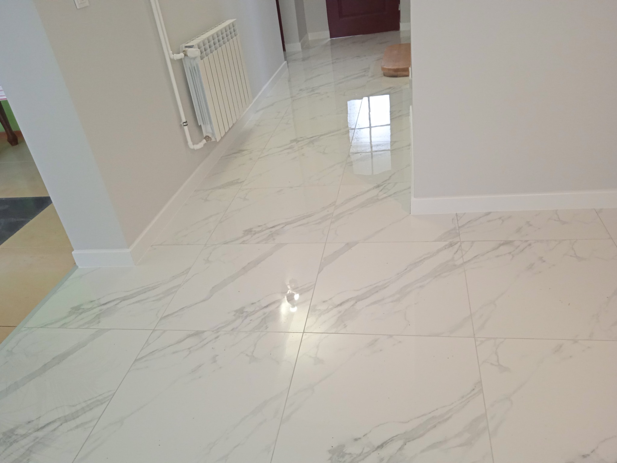 Biała marmurowa podłoga w korytarzu z grzejnikiem na ścianie i widocznym fragmentem drzwi w tle.