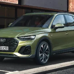 Zielony SUV Audi Q5 z polską tablicą rejestracyjną PO GCZ20 zaparkowany na ulicy z ceglanym budynkiem w tle.