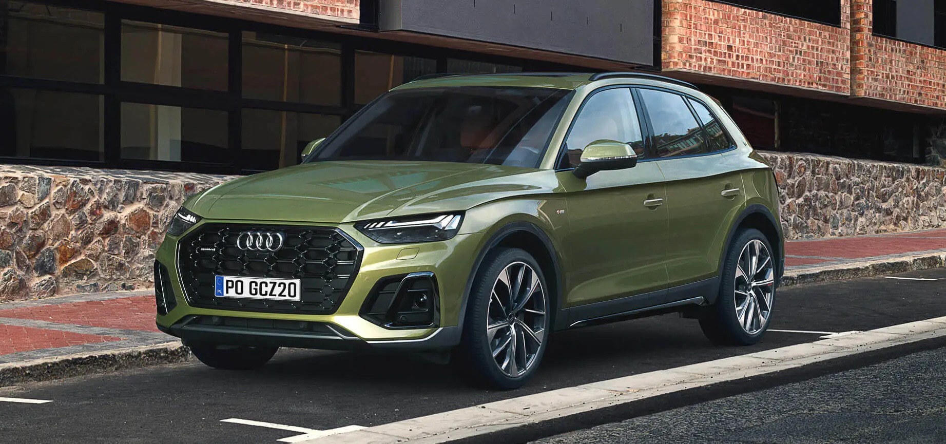 Zielony SUV Audi Q5 z polską tablicą rejestracyjną PO GCZ20 zaparkowany na ulicy z ceglanym budynkiem w tle.