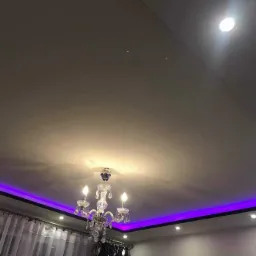 Sufit z kryształowym żyrandolem i podświetleniem LED w kolorze fioletowym, widoczne również punktowe źródła światła.