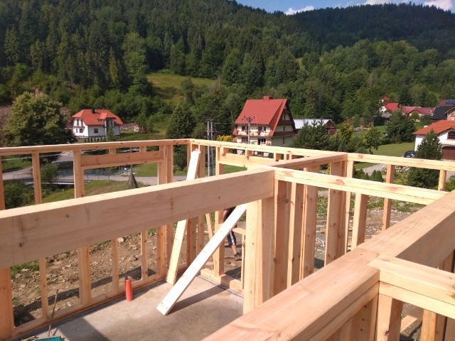 Konstrukcja drewniana domu w stanie surowym otwartym na tle górskiego krajobrazu z zabudowaniami.