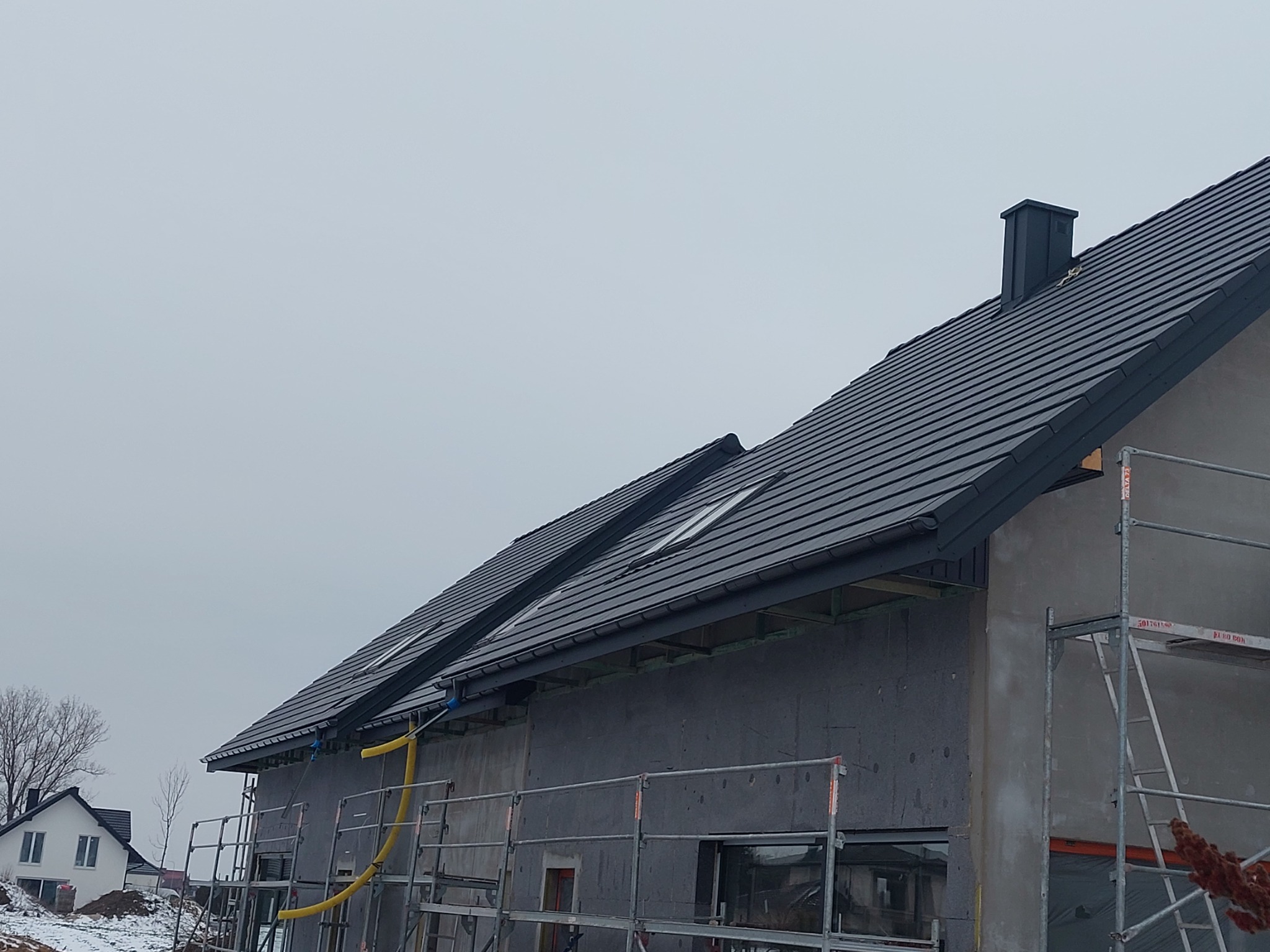 Nowy, grafitowy dach z oknami połaciowymi i kominem na domu w trakcie budowy w Lublinie, widok z rusztowania.