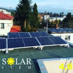 Instalacja paneli słonecznych na płaskim dachu budynku z widocznym logo firmy 'Eco Solar System' i informacją o mocy 4.69kW, w tle zabudowa mieszkalna i drzewa.