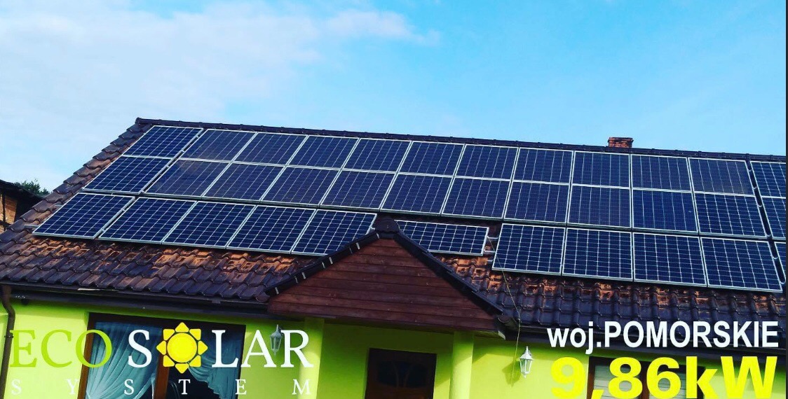 Instalacja paneli fotowoltaicznych na dachu domu jednorodzinnego, widok z dołu, z widocznym fragmentem elewacji z logo firmy Eco Solar System i informacją o lokalizacji 'woj. Pomorskie' oraz mocy...