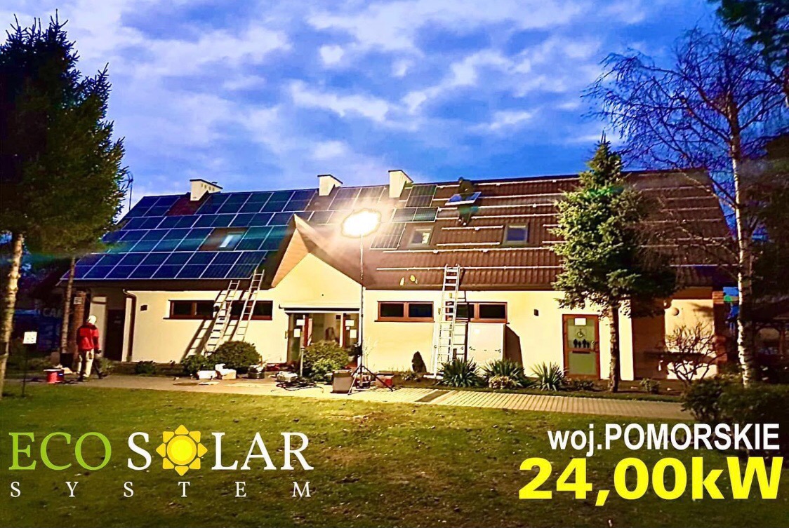 Montaż paneli słonecznych na dachu dwukondygnacyjnego budynku w województwie pomorskim, widoczny pracownik na dachu oraz logo firmy Eco Solar System na trawniku.