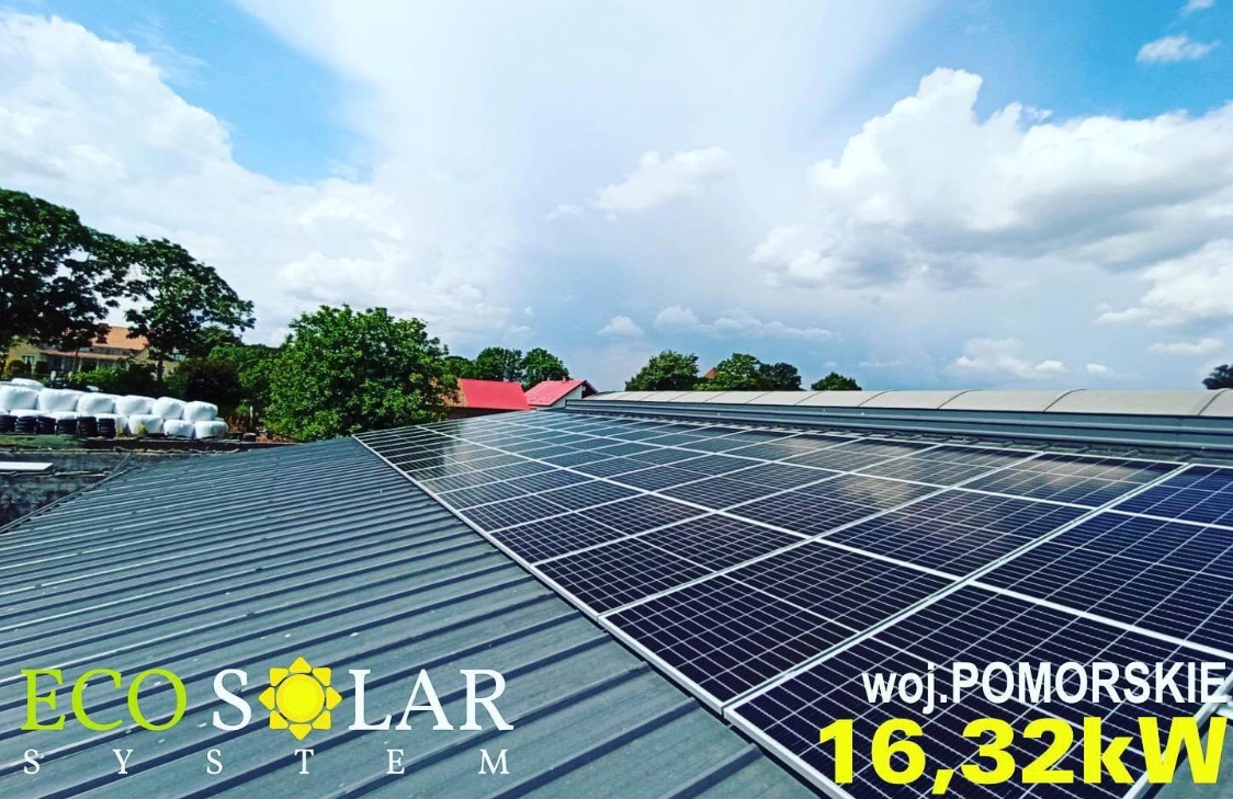 Panel słoneczny na metalowym dachu budynku gospodarczego, widok z dołu na tle błękitnego nieba z chmurami. Na pierwszym planie logo firmy i informacja o mocy instalacji w województwie pomorskim.