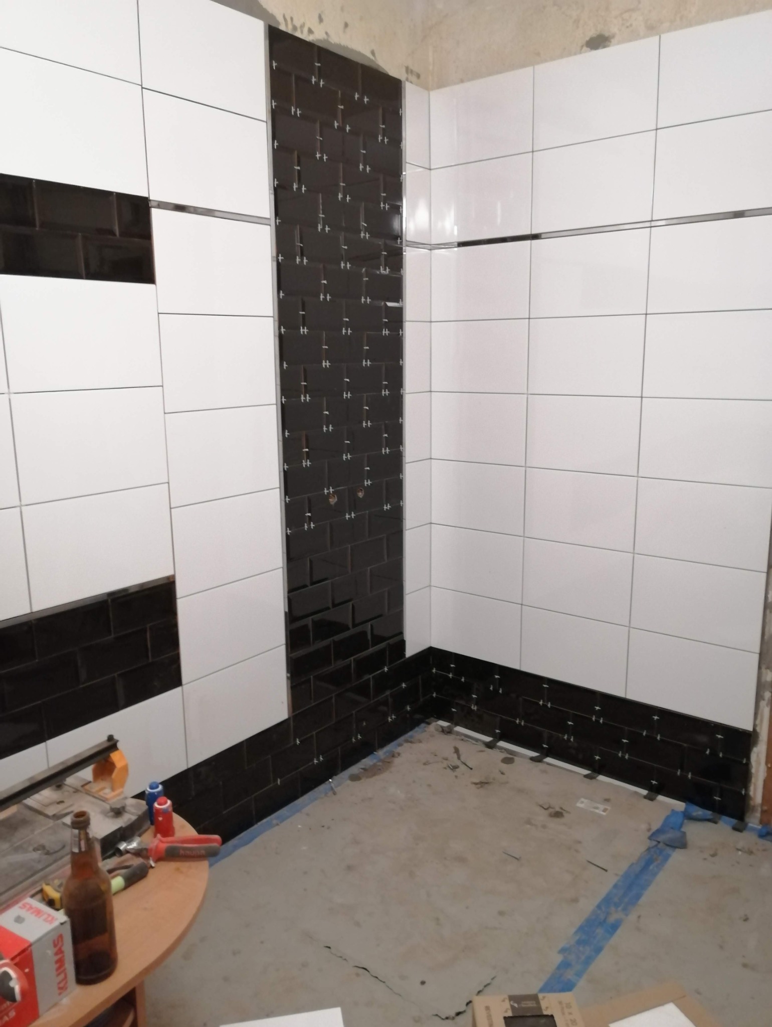 Układanie czarnych i białych płytek w łazience, widoczne krzyżyki dystansowe, narzędzia i materiały budowlane na stole