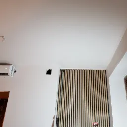 Fragment wnętrza z panelami dekoracyjnymi na ścianie, widoczny otwór po gniazdku elektrycznym i klimatyzator na ścianie obok.