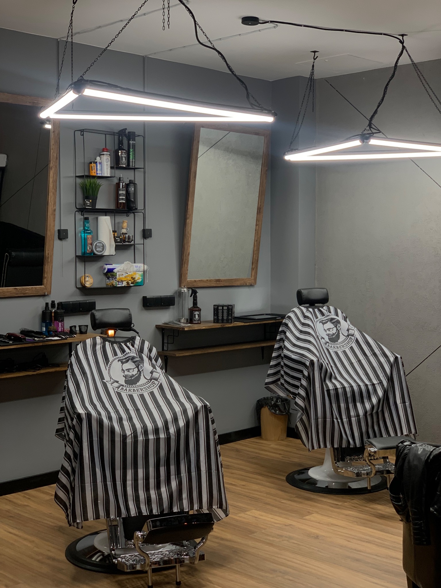 Nowoczesne wnętrze salonu barberskiego z dwoma fotelami w czarno-białe pasy, oświetleniem LED i minimalistycznymi półkami z kosmetykami.