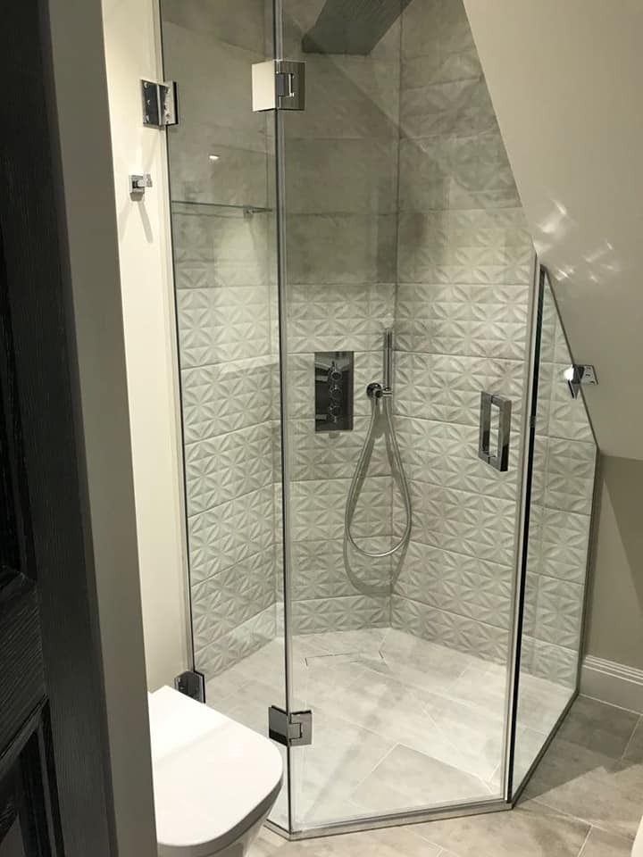 Nowoczesna kabina prysznicowa z geometrycznymi płytkami na ścianach, zamontowana w łazience na poddaszu ze skośnym sufitem, widoczna toaleta z lewej strony.