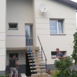 GERARD-PRO USŁUGI RMONTOWO-BUDOWLANE MICHAŁ BZICKI - Dwóch pracowników w Ciecierzynie przygotowuje się do malowania elewacji dwupiętrowego domu z betonowymi schodami wejściowymi, widoczna satelita na ścianie.