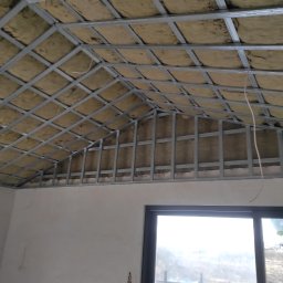 GERARD-PRO USŁUGI RMONTOWO-BUDOWLANE MICHAŁ BZICKI - Skośny sufit poddasza z widoczną konstrukcją metalową i izolacją z wełny mineralnej, przygotowany do montażu płyt karton-gips.