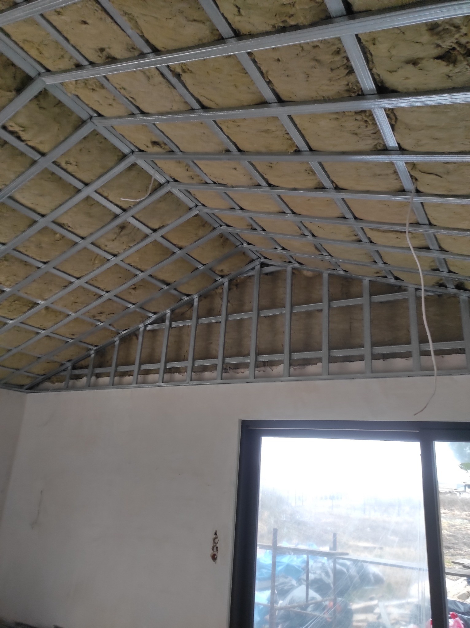 Skośny sufit poddasza z widoczną konstrukcją metalową i izolacją z wełny mineralnej, przygotowany do montażu płyt karton-gips.
