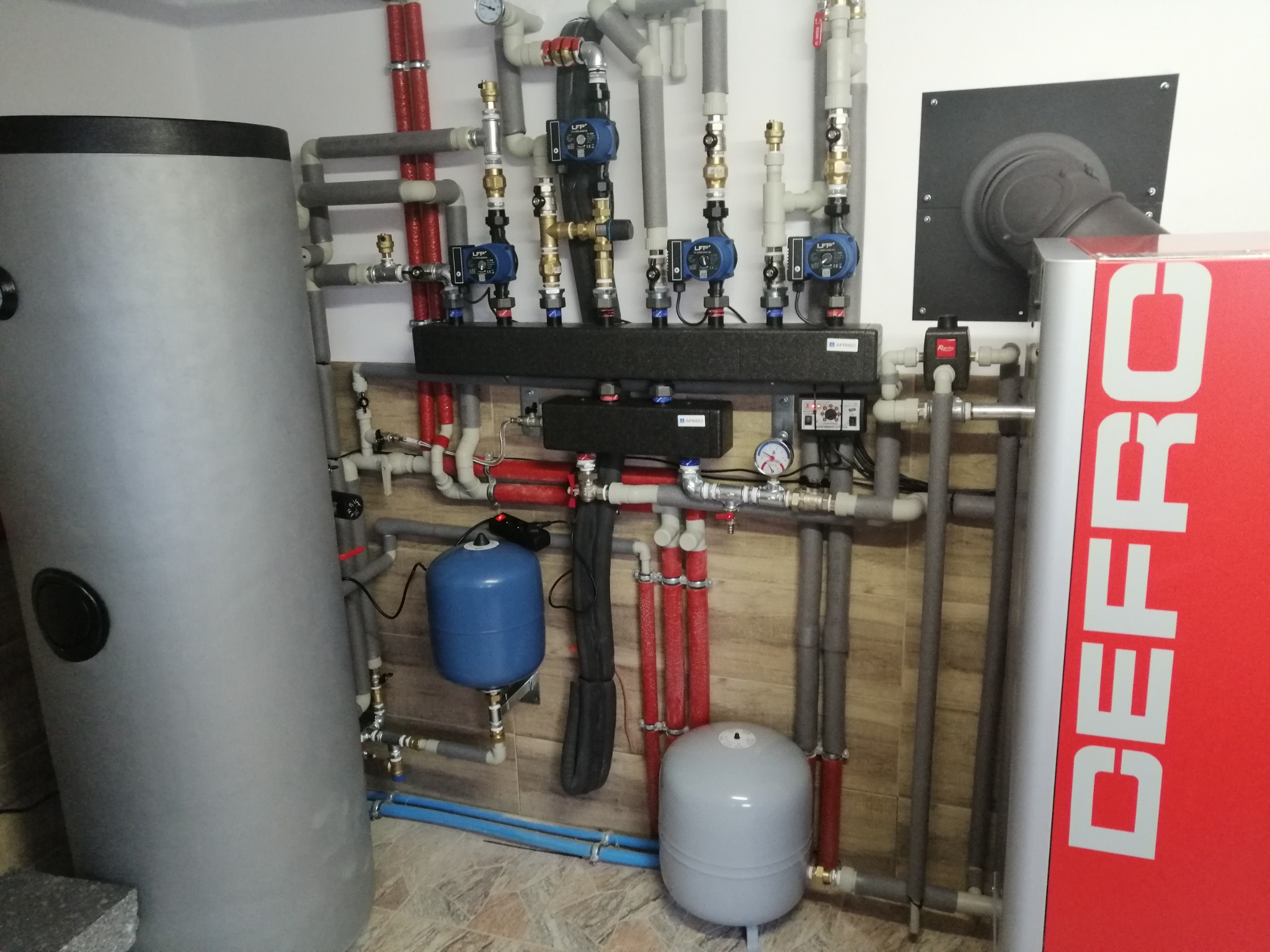 Węzeł cieplny z zbiornikiem akumulacyjnym, kotłem DEFRO, pompami obiegowymi LFP i licznymi rurami w instalacji grzewczej.