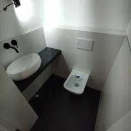 Nowoczesna, wąska łazienka z białymi płytkami, wiszącą miską WC, umywalką nablatową na blacie imitującym czarny marmur i czarną armaturą.