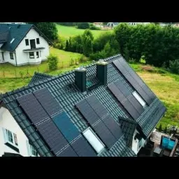 Widok z góry na dom z zainstalowanymi panelami fotowoltaicznymi na dachu, z widocznym drugim budynkiem w tle.
