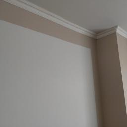 MJColors - Pomieszczenie po remoncie: ściana w kolorze złamanej bieli z beżowym pasem pod sufitem i białym, ozdobnym gzymsem.