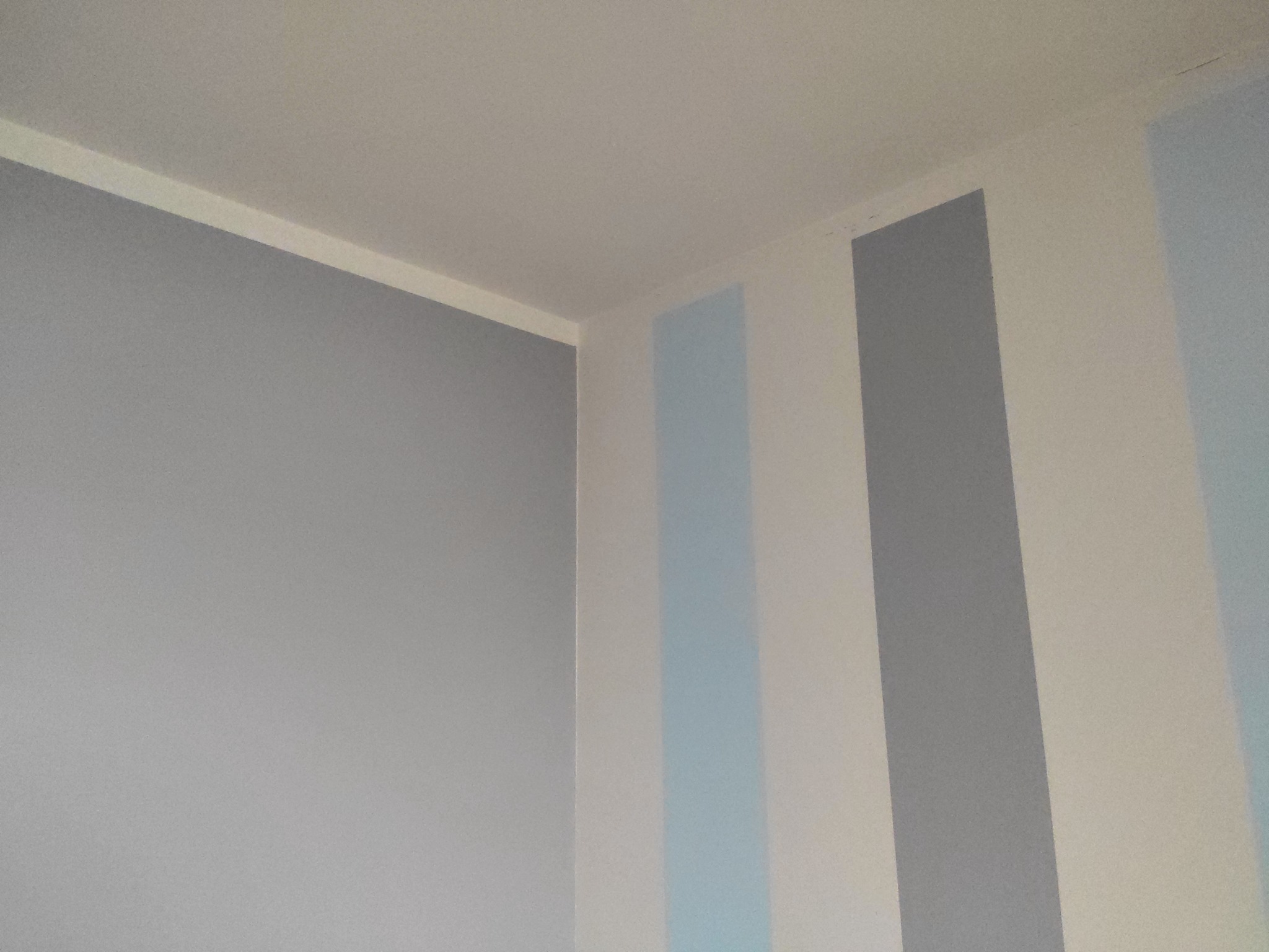 Świeżo pomalowany narożnik pokoju z pionowymi pasami w odcieniach szarości i błękitu na białym tle.