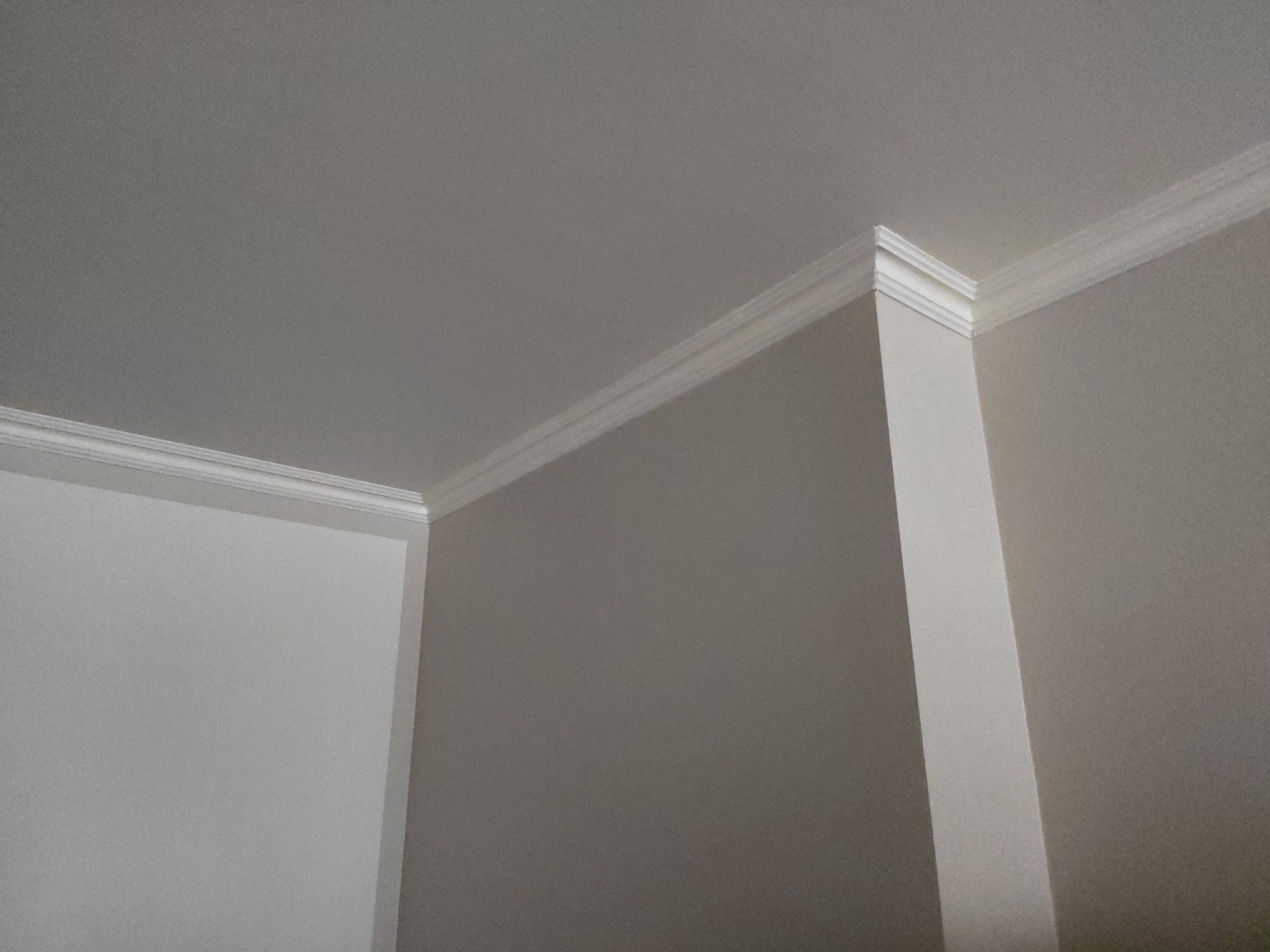 Wnętrze po odświeżeniu: Jasnoszara ściana i biały sufit z dekoracyjną listwą przysufitową, widok na narożnik pomieszczenia.