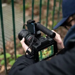 Operator kamery z profesjonalnym sprzętem nagrywającym leśny krajobraz, widoczny na ekranie podglądowym.
