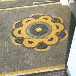 Ułożona kostka brukowa w kształcie kwiatu z szarych, żółtych, brązowych i czarnych kostek, obok budynku.