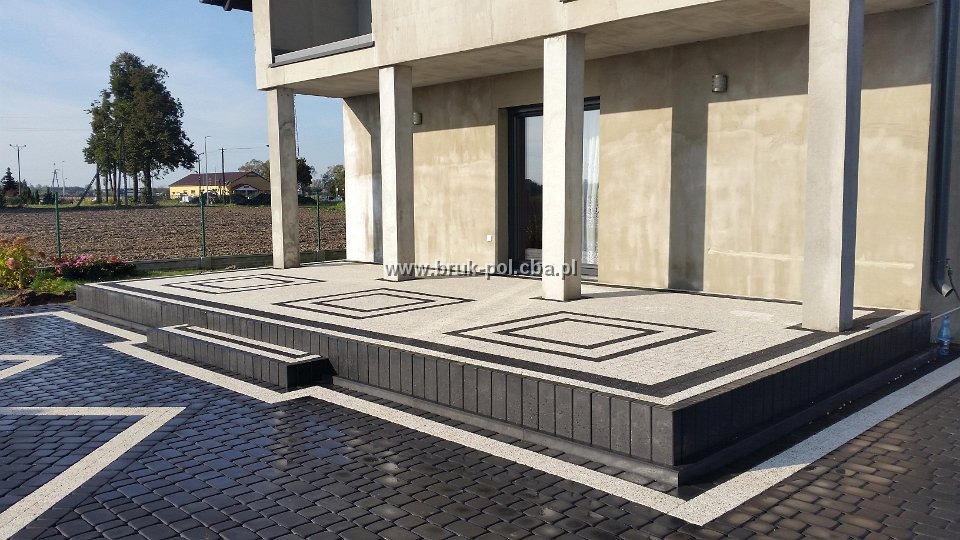 Nowoczesny taras z kostki brukowej w geometryczne wzory, czarno-biała kompozycja, widok na dom z kolumnami.