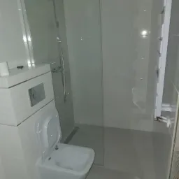 Nowoczesna łazienka z kabiną prysznicową typu walk-in, podwieszaną toaletą i grzejnikiem drabinkowym, wykończona w jasnych odcieniach szarości i bieli.