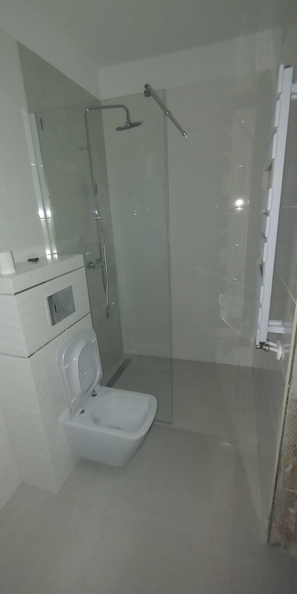 Nowoczesna łazienka z kabiną prysznicową typu walk-in, podwieszaną toaletą i grzejnikiem drabinkowym, wykończona w jasnych odcieniach szarości i bieli.