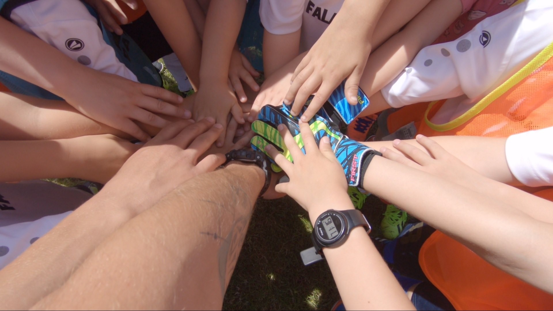 Grupowe ułożenie dłoni na dłoniach, w centrum rękawice bramkarskie i zegarek sportowy, symbol zjednoczenia drużyny na kolonii lub obozie.