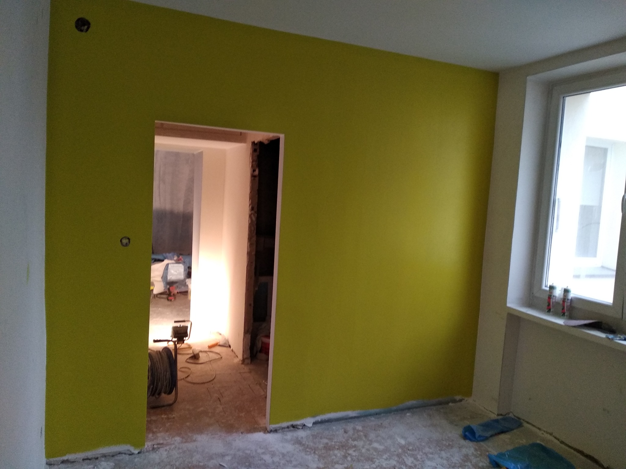Świeżo pomalowany pokój na żółto, widoczne narzędzia malarskie i surowy stan podłogi przed dalszym wykończeniem.