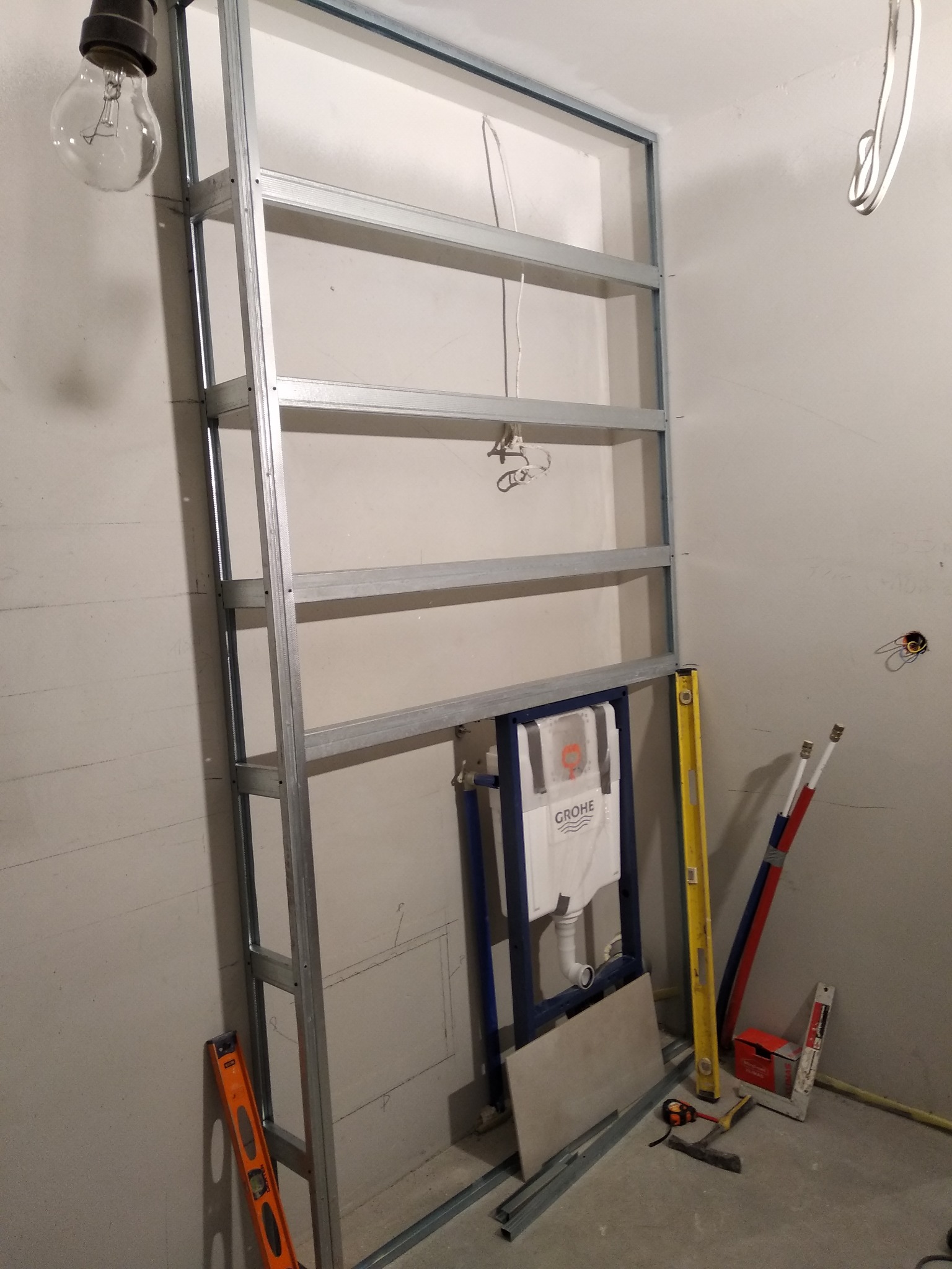 Stelaż metalowy pod zabudowę WC z zamontowanym modułem Grohe, poziomica i narzędzia w surowym wnętrzu łazienki w trakcie prac wykończeniowych.